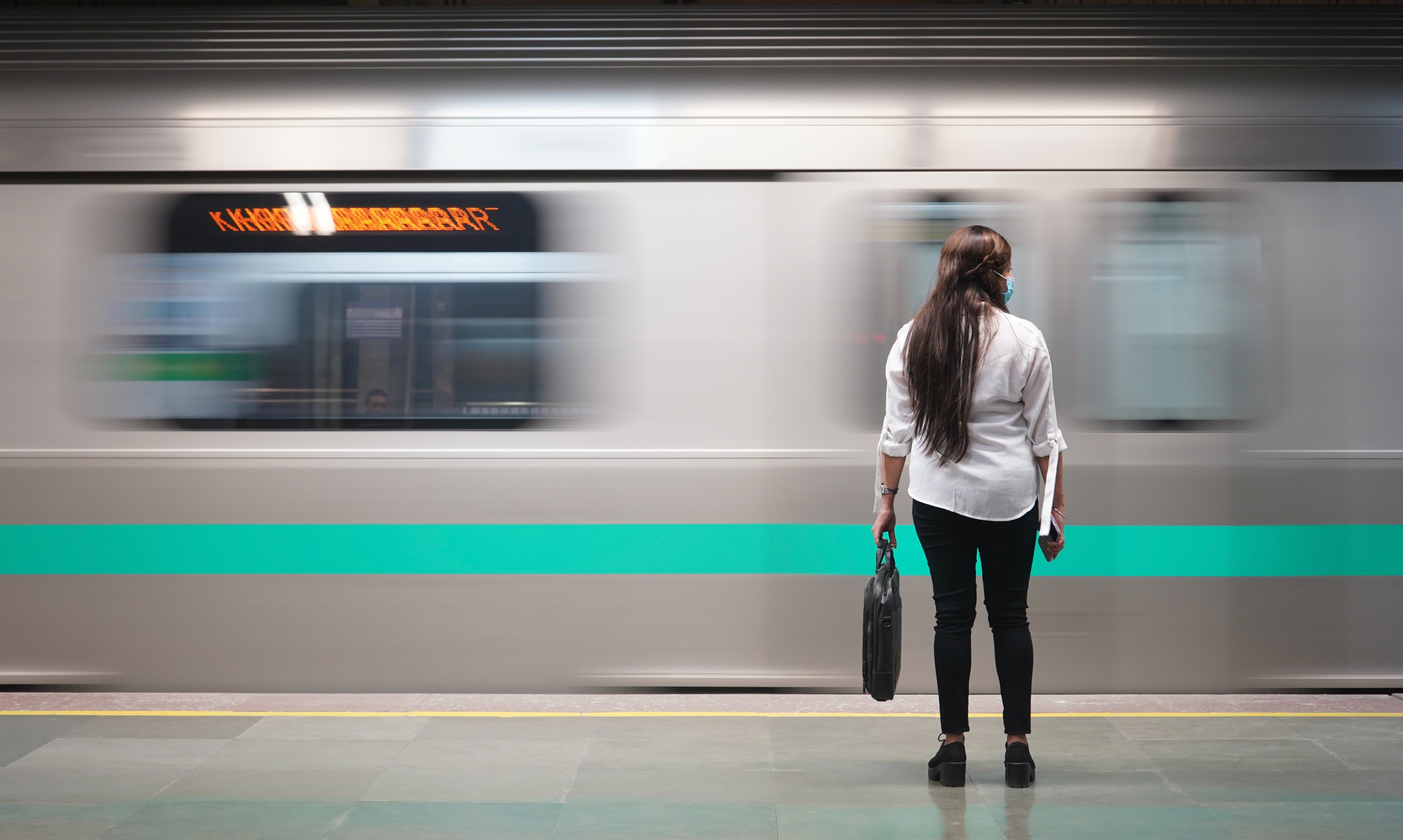 A woman in business attire stands on a train platform while a blurred train passes in front of her. 