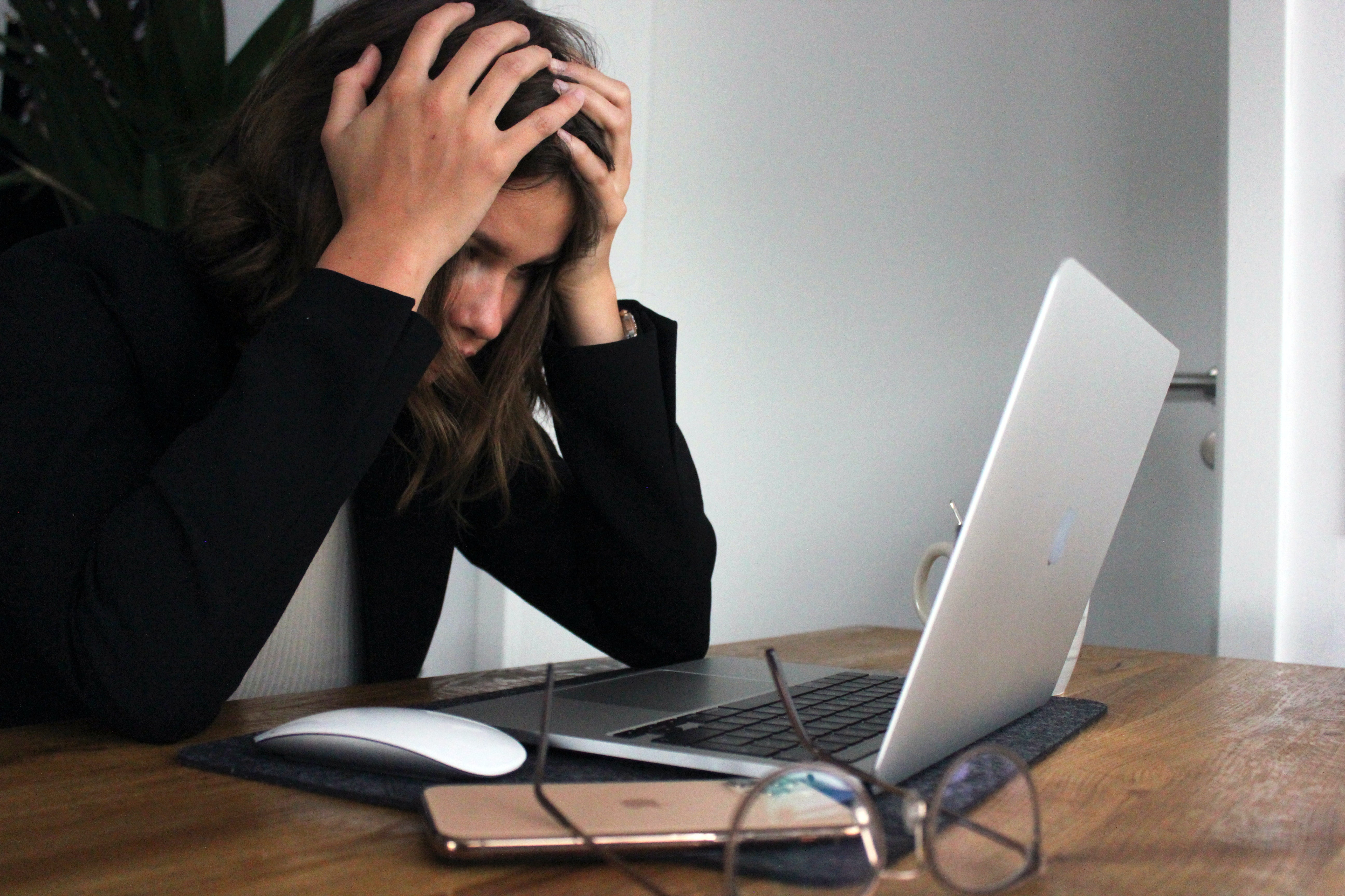 Woman hold her head in her hands and looks down at a computer screen.