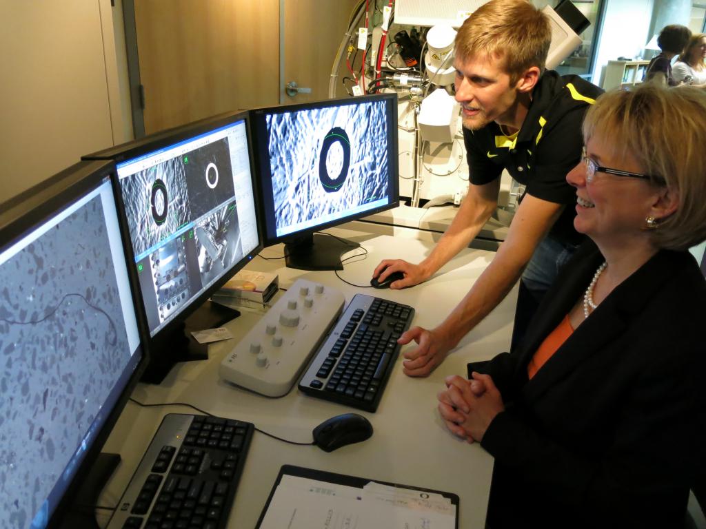 Two people look at microscopic images across three computer screens in the CAMCOR lab.