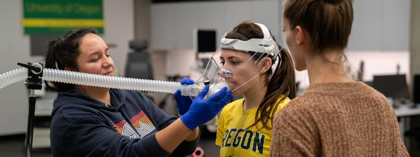 A woman fits a research subject with a face mask attached to a tube to monitor oxygen use during a treadmill test.