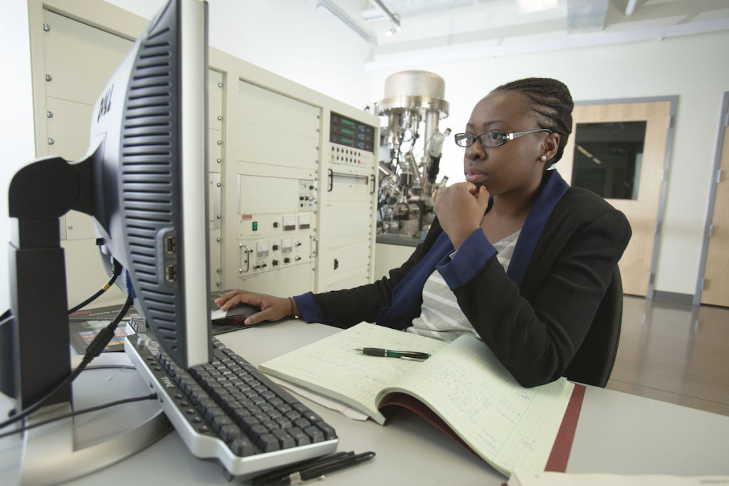 A person works on a computer in the CAMCOR facilities. A notebook is open in front of them.