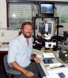 Ted Fremd poses in front of a microscope.