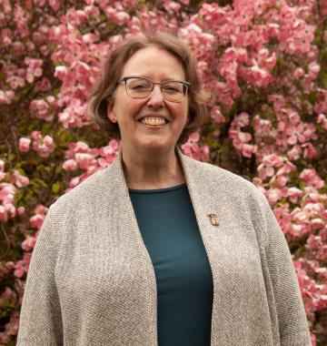 A woman smiles for the camera, standing in front of pink flowers