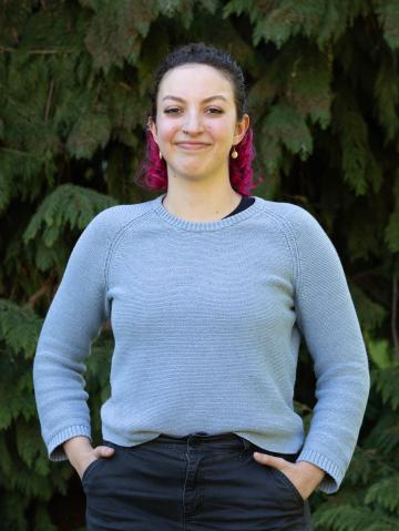 A woman stands with her hands in her pockets in front of a tree